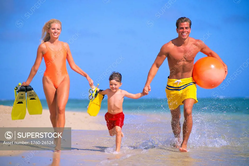 Front view of young family running along shoreline with snorkel gear, ball, C1085 blue sky