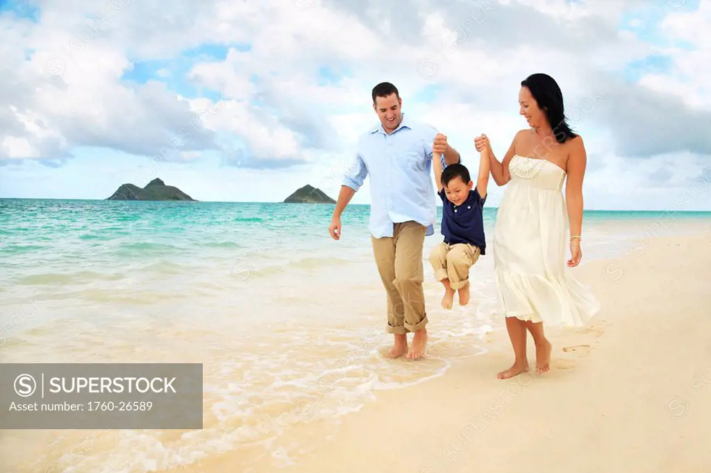 Hawaii, Oahu, Lanikai, Young Family holding hands strolling along the beach.