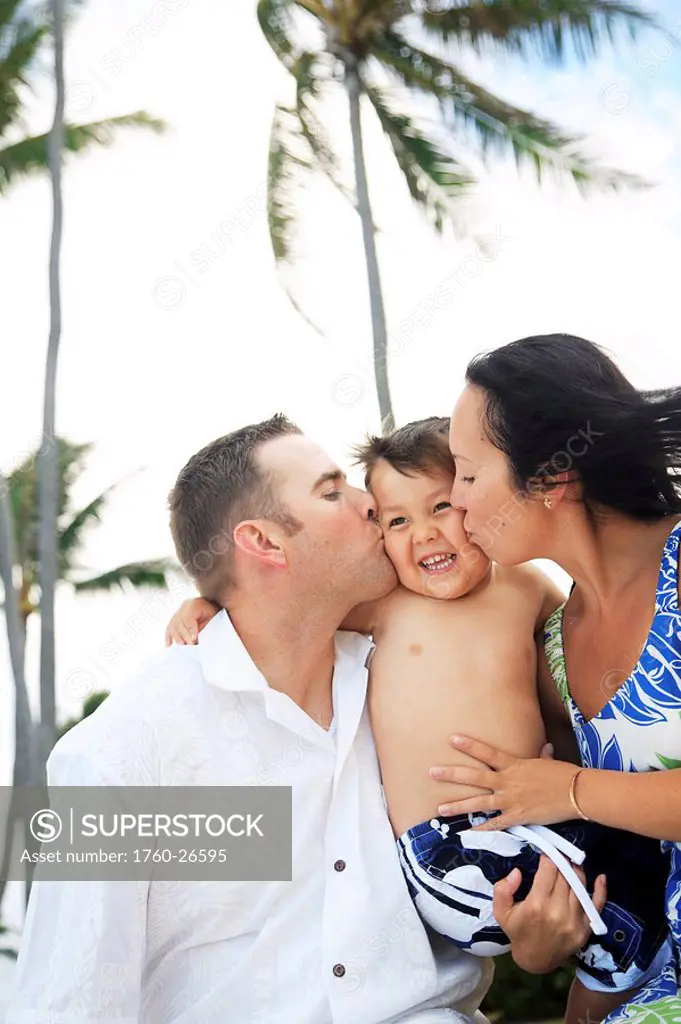 Hawaii, Oahu, Loving moment of Parents kissing their young son on his cheeks.