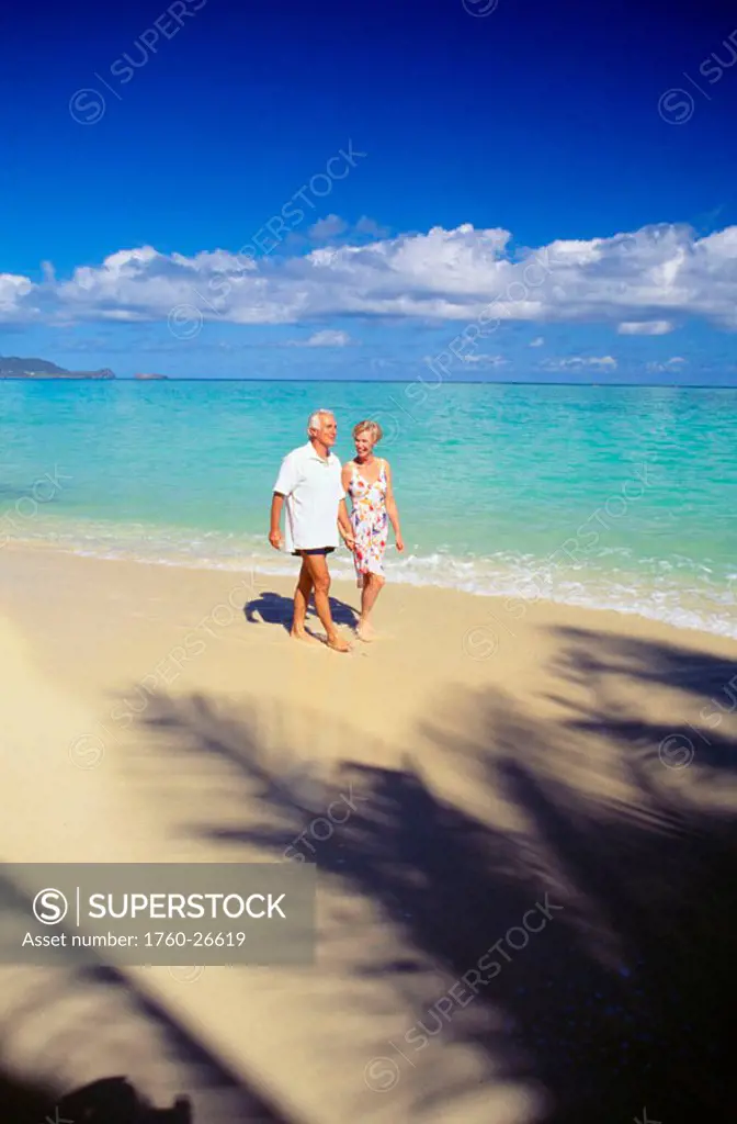 Senior couple walks along shoreline, blue sky, turquoise ocean, white sand