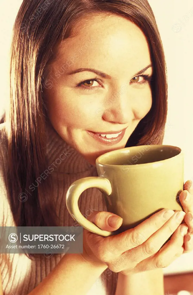 Smiling woman holding a mug up, about to drink. Warm light. Posed.