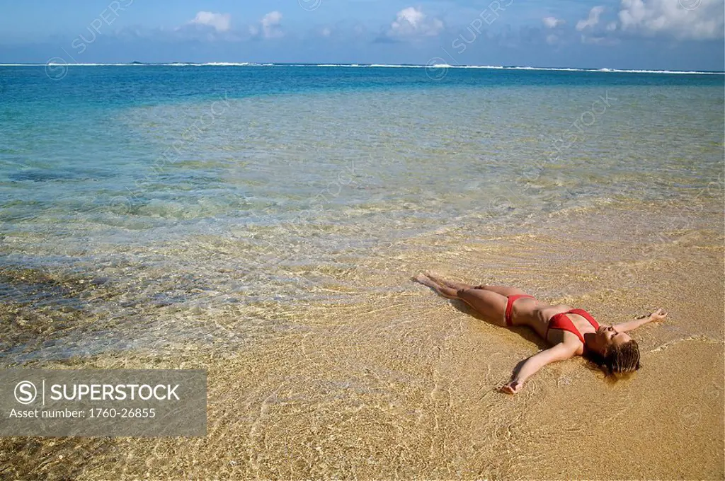 Hawaii, Kauai, Kealia beach, Woman laying on the beach in the shoreline.