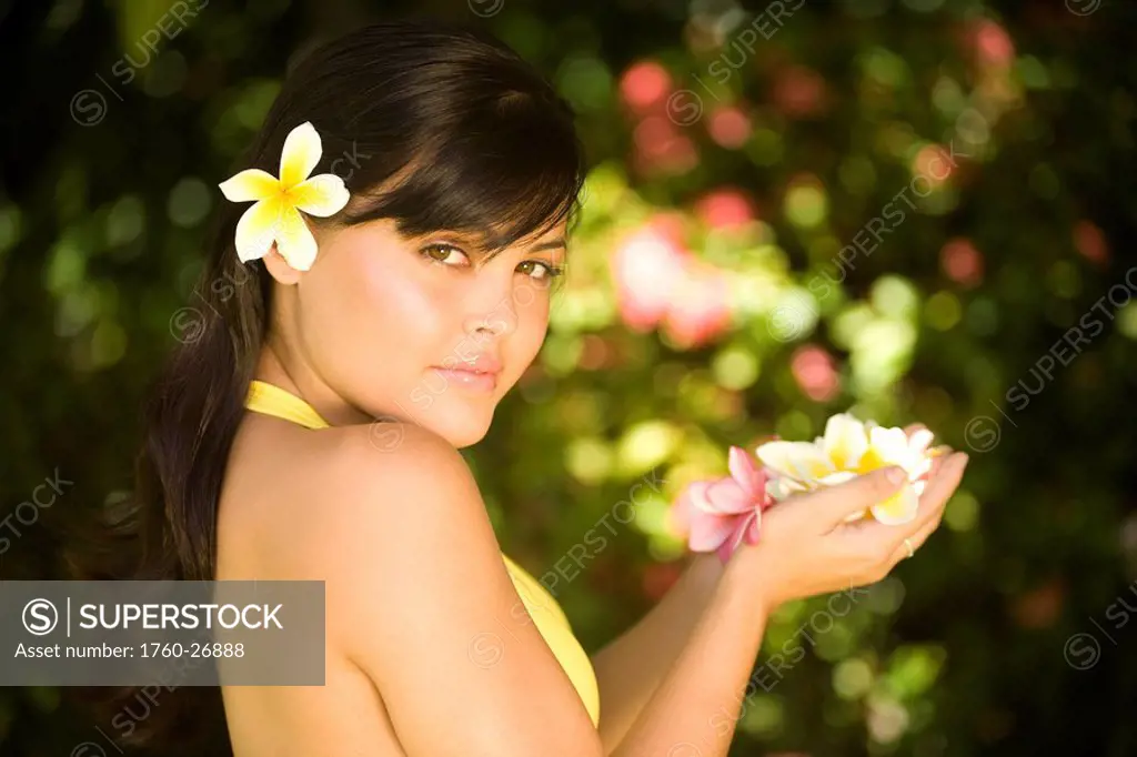 Hawaii, Oahu, Beautiful headshot of a young girl with a plumeria in her ear, holding plumerias in her hand.