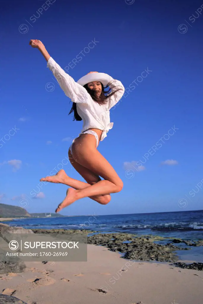 Young woman jumping in air, thong bikini, white top and white hat