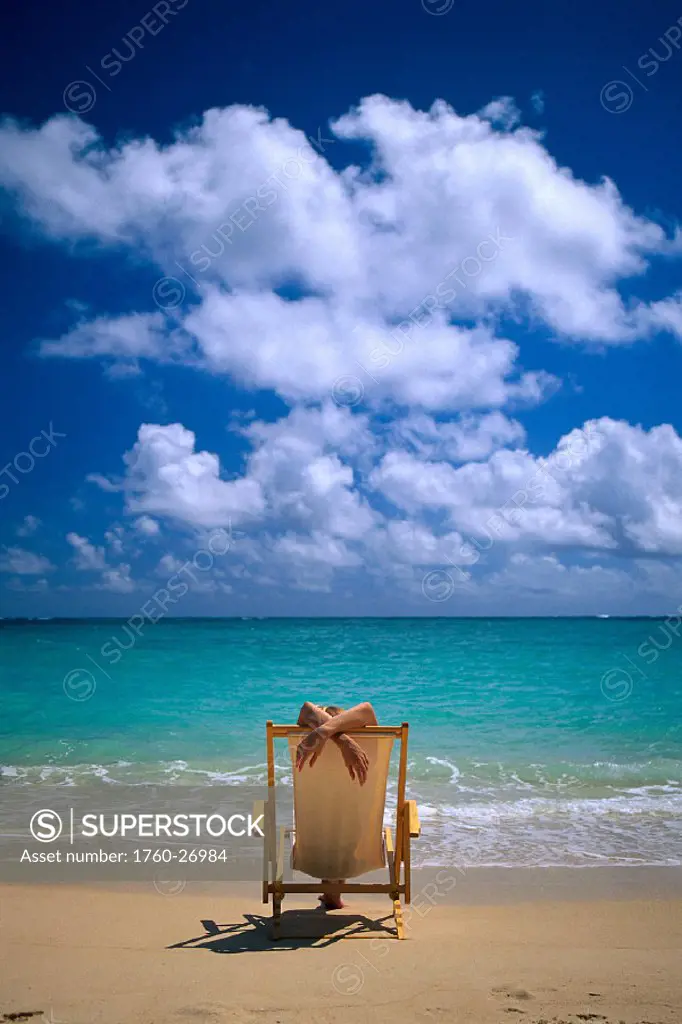 Woman lounging in beach chair face water, arms cross over back, fr behind B1069