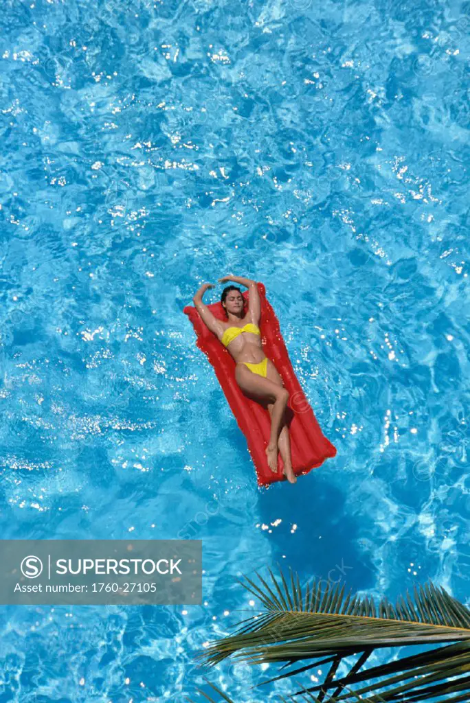 View fr above woman in pool laying on red air mattress, w/ yellow swimsuit