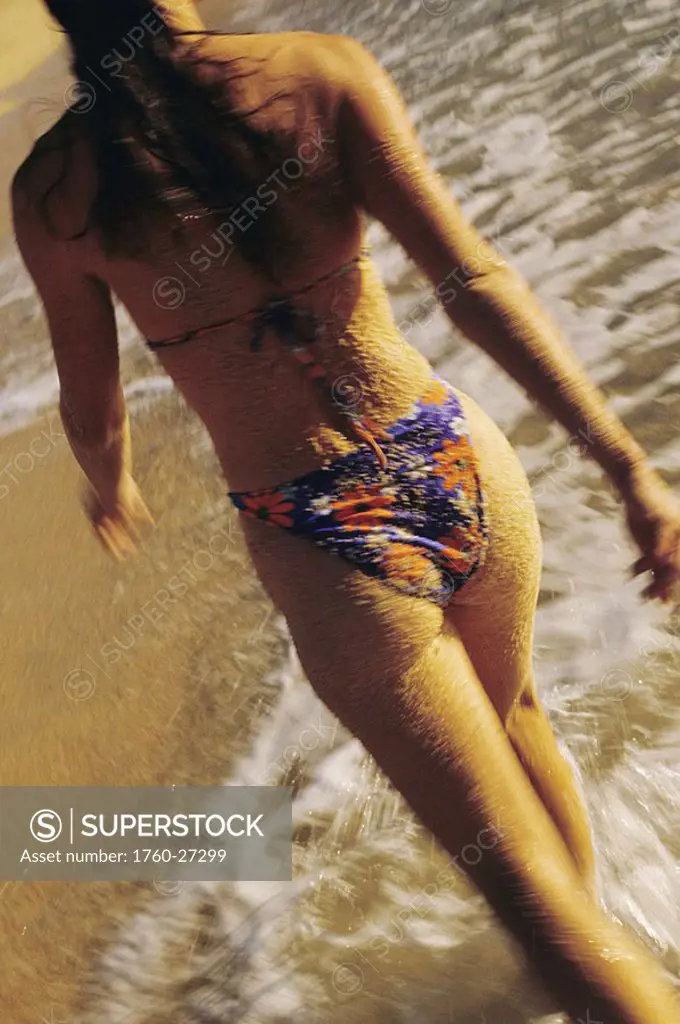 Mexico, Cabo San Lucas, Close-up of woman walking in ocean along beach, View from behind