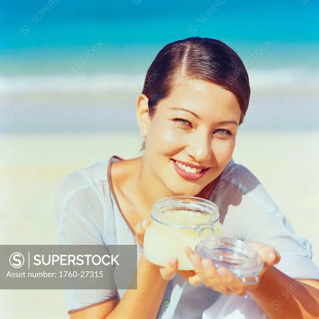 Young woman smelling jar of beauty cream on the beach.