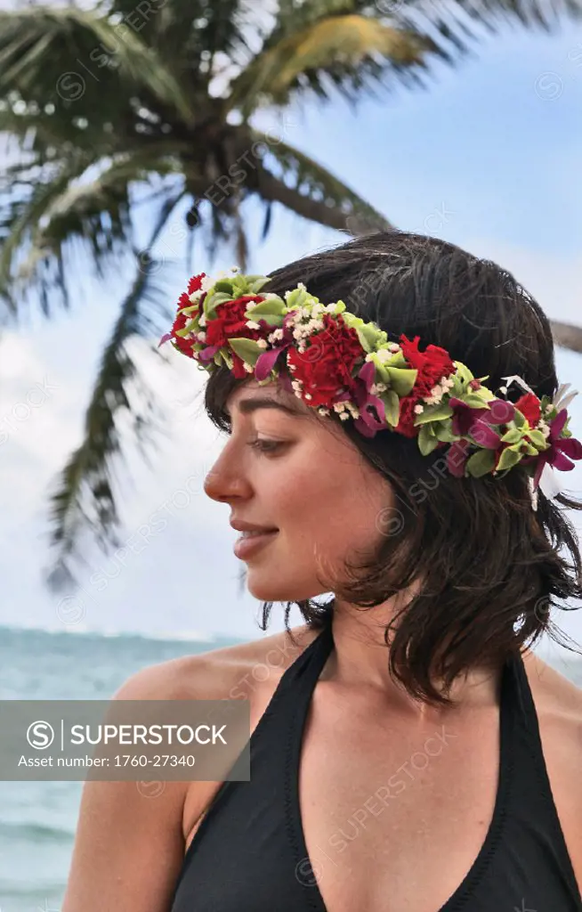 Hawaii, Oahu, Beautiful woman wearing haku lei by the ocean looks to the side.
