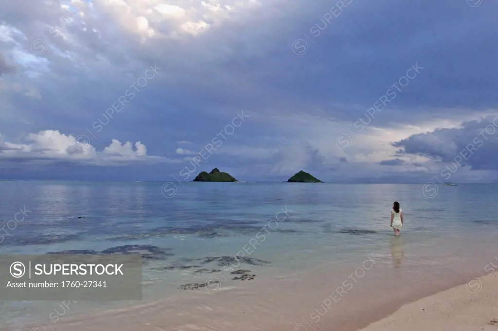 Hawaii, Oahu, Lanikai, a woman wades in the water at the beach at dusk.