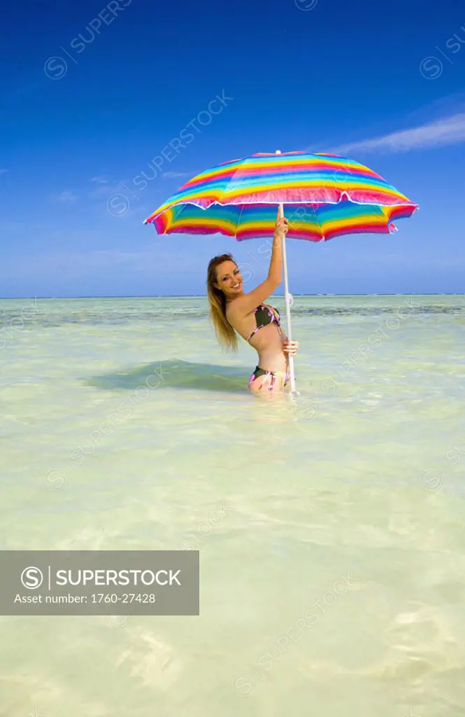 Hawaii, Oahu, Kaneohe, Woman standing under a brightly colored umbrella in crystal clear water at the sandbar or ´dissapearing island´