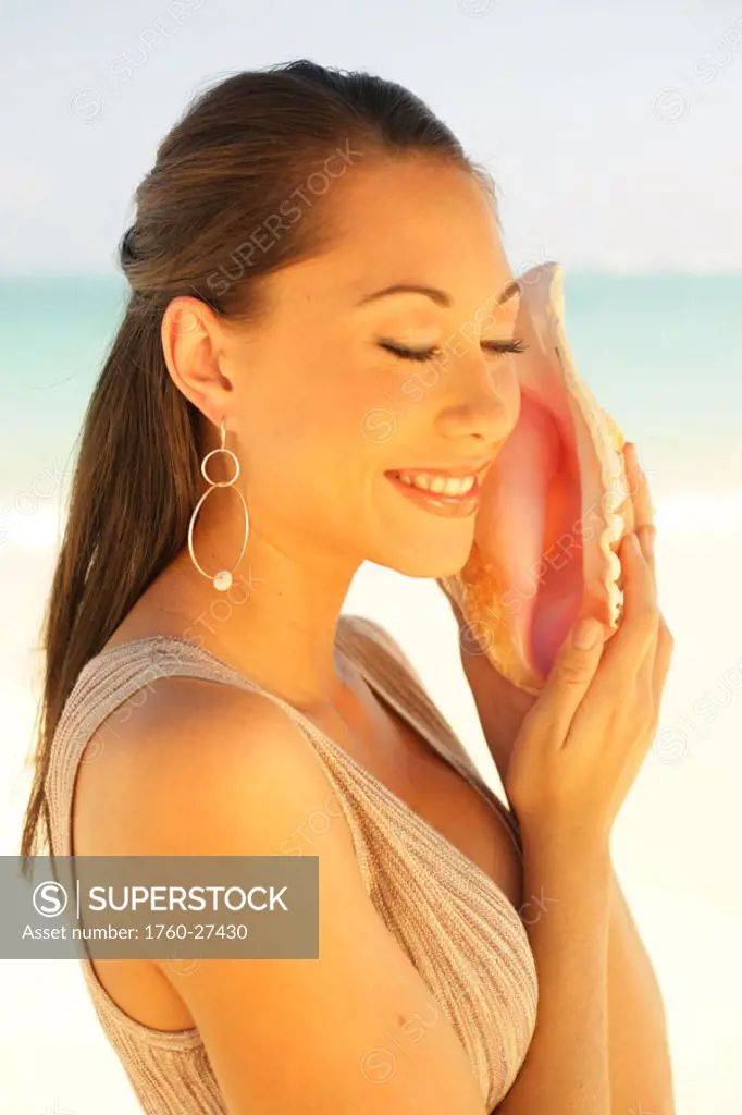 Hawaii, Beautiful sophisticated girl listens to a seashell.