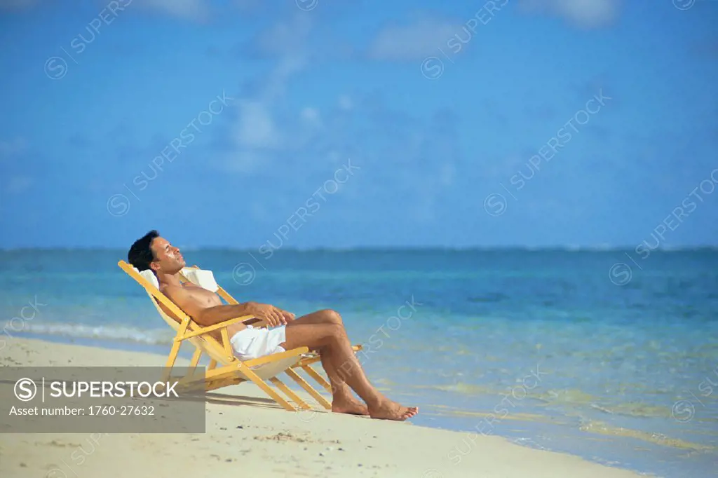 Man laying along shoreline waters, relaxing in lounge chair C1122