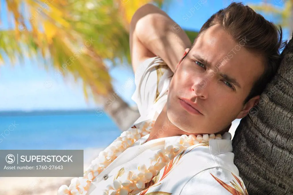 Hawaii, Oahu, European male leaning against a palm tree and relaxing at a tropical beach.
