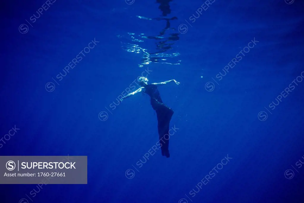 Surreal view of woman wearing an evening gown underwater posing surface reflections and sunrays abstract strange