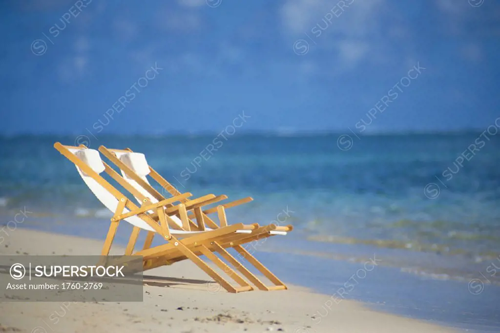 Closeup of two beach chairs on shoreline, clear water, blue sky C1696