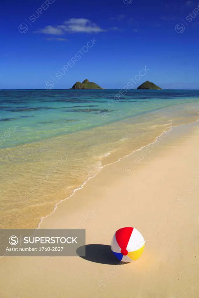 Hawaii, Oahu, Lanikai, Colorful beachball on the shore of tropical beach, Mokulua islands in background.