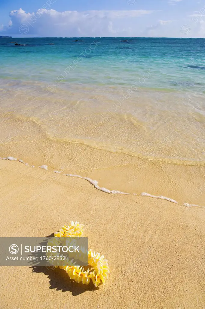 Hawaii, Oahu, Lanikai Beach, turquoise ocean with yellow plumeria lei laying on the sand.