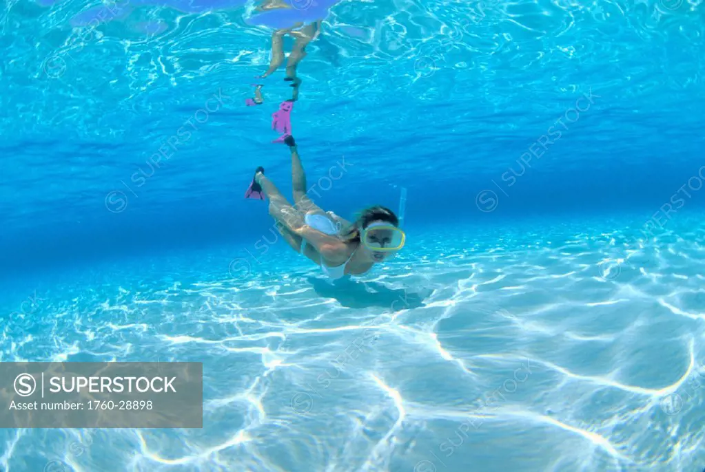 Woman snorkeler near surface u/w in clear turquoise water sun reflections on sandy bottom