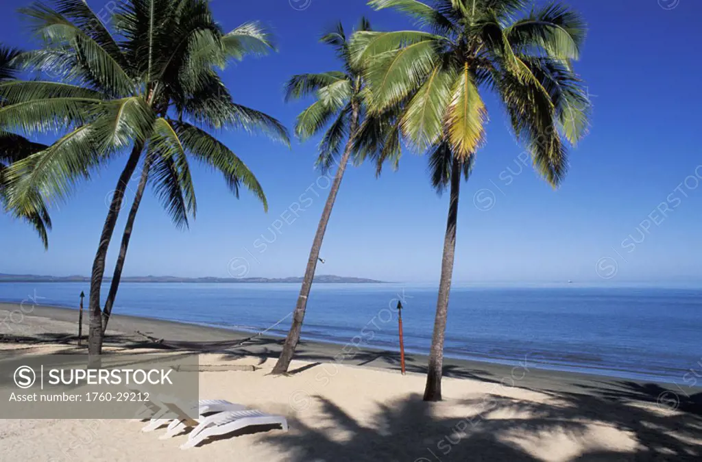 Fiji, Nadi Bay, Sheraton resort, white chairs on sandy beach, palm trees and shadows.