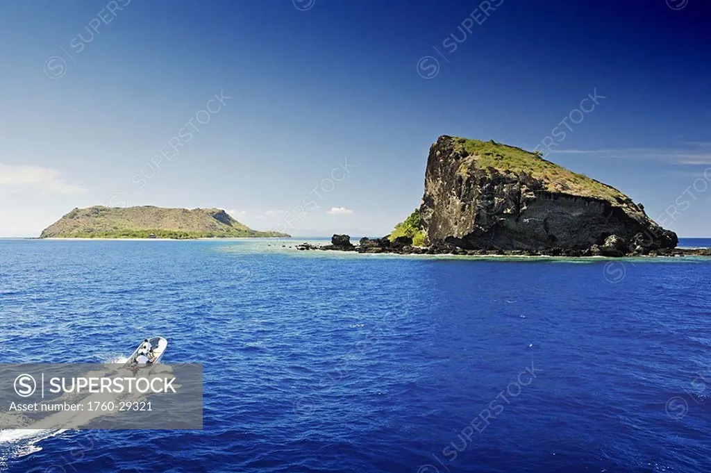 Fiji, Mamanuca Islands, small boat approaching Vomo Island, home of Sofitel Resort, dramatic rock formation in foreground, view from ocean