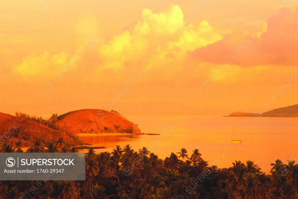 Fiji, Mana Island, sailboat in calm bay waters, orange pink skies w/ puffy clouds