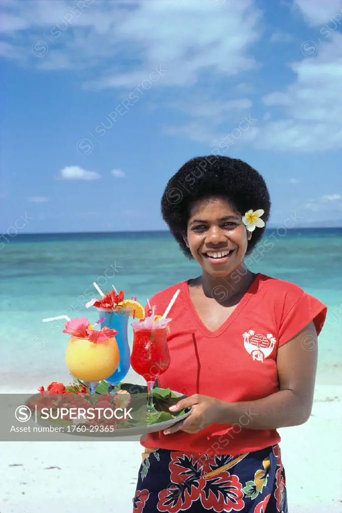 Fiji, Nadi, Fijian waitress holds tray of tropical drinks, shoreline of beach
