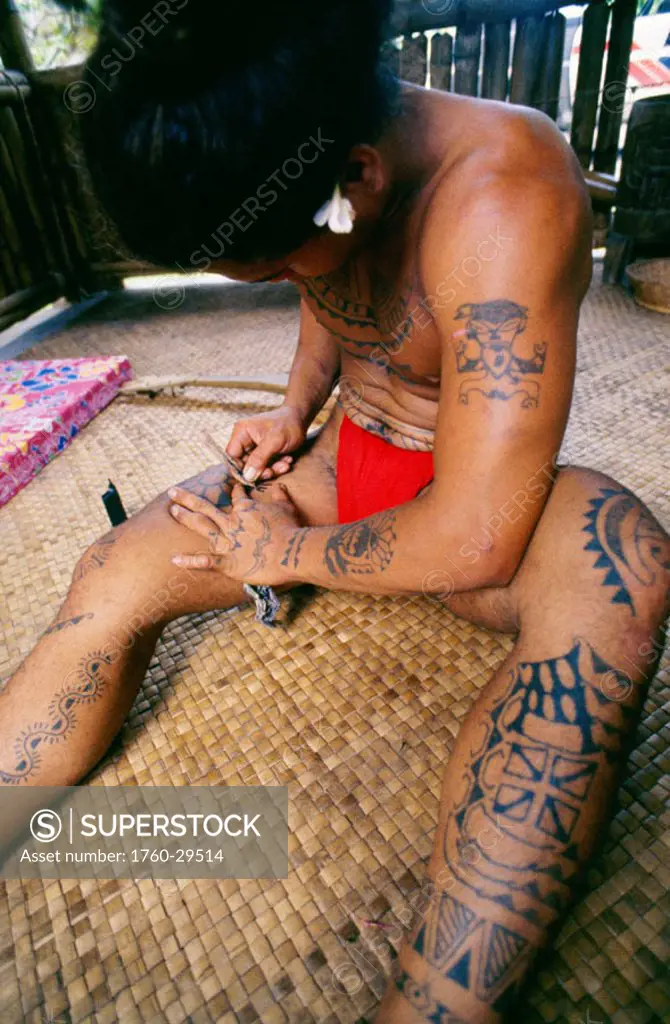 French Polynesia, Huahine, Polynesian man tatooing his thigh, sitting on thatched rug