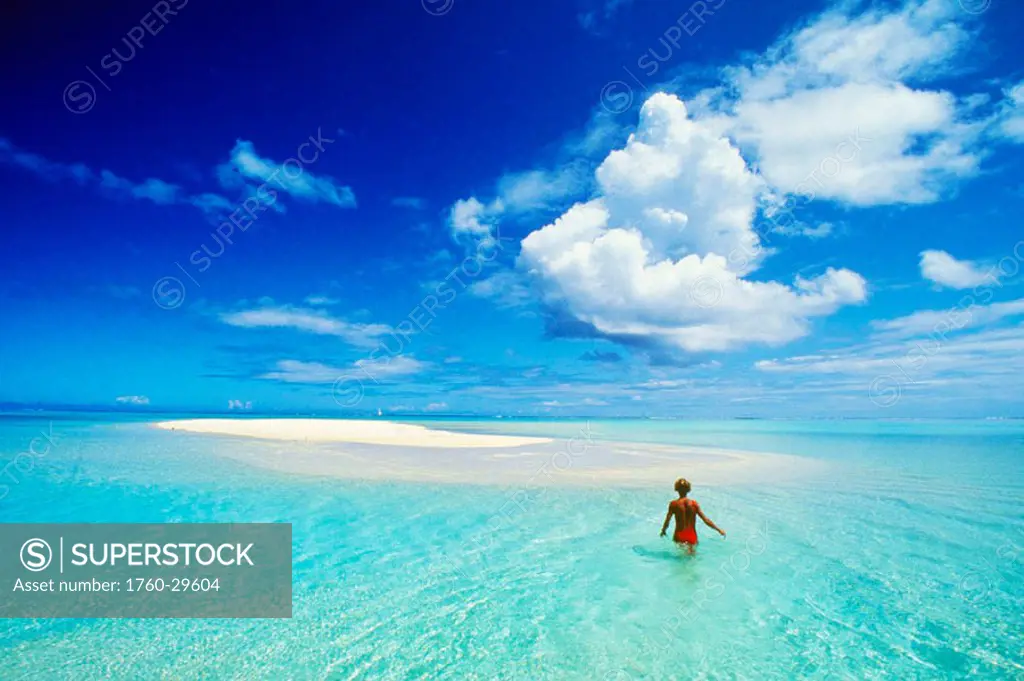 French Polynesia, Tahiti, Bora Bora, calm turquoise ocean surrounds sand islet, woman wading, view from behind