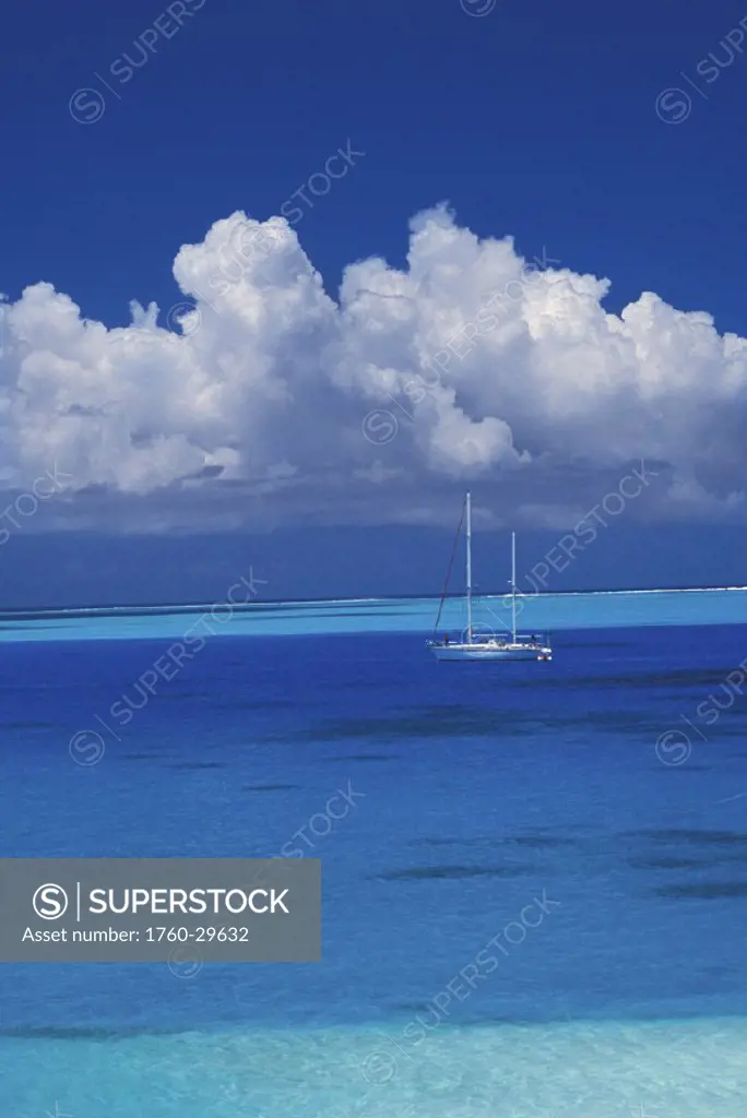 French Polynesia, Bora Bora, Sailboat on clear turquoise ocean with billowing cumulous clouds