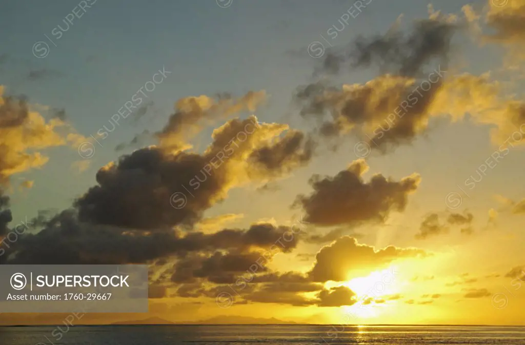 French Polynesia, Raiatea, Sun shining through clouds over the ocean at sunset