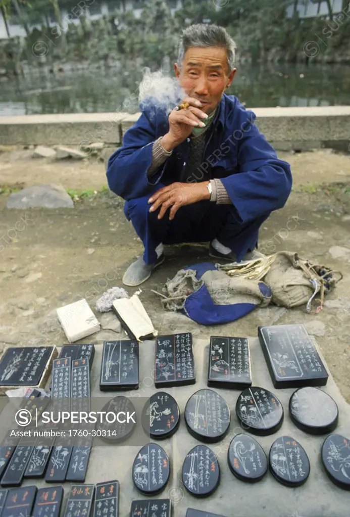 China, Canton, Chinese vendor selling calligraphy stones, squatting and smoking NO MODEL RELEASE