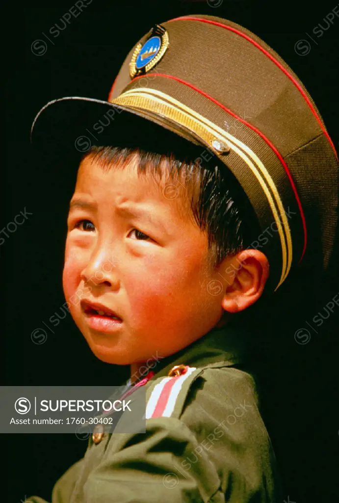 China, portrait shot of young boy in military uniform, black background
