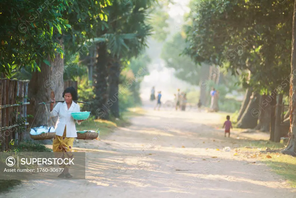 Cambodia, Woman carrying her goods down a dirt road.