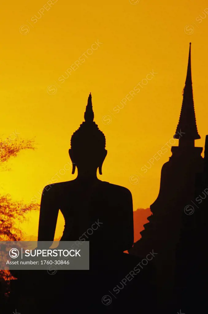 Thailand, Sukhothai, Buddha and temple silhouetted at sunset, orange sky