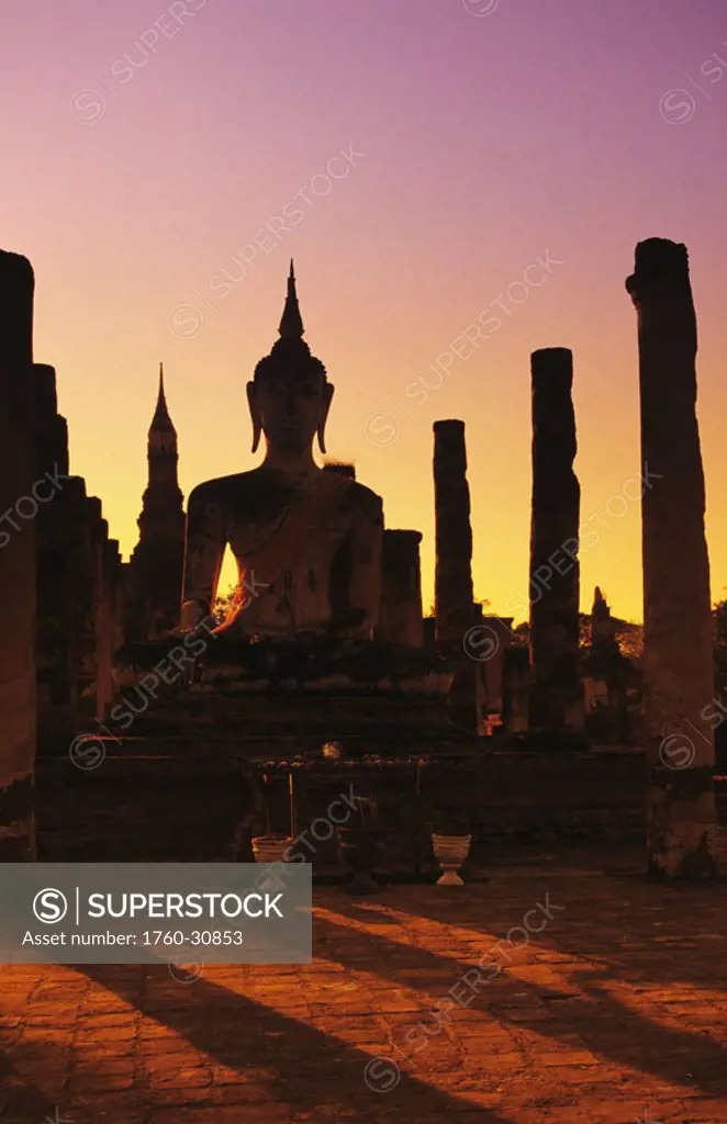 Thailand, Sukhothai, Wat Mahathat, Buddha and pillars backlit at sunset