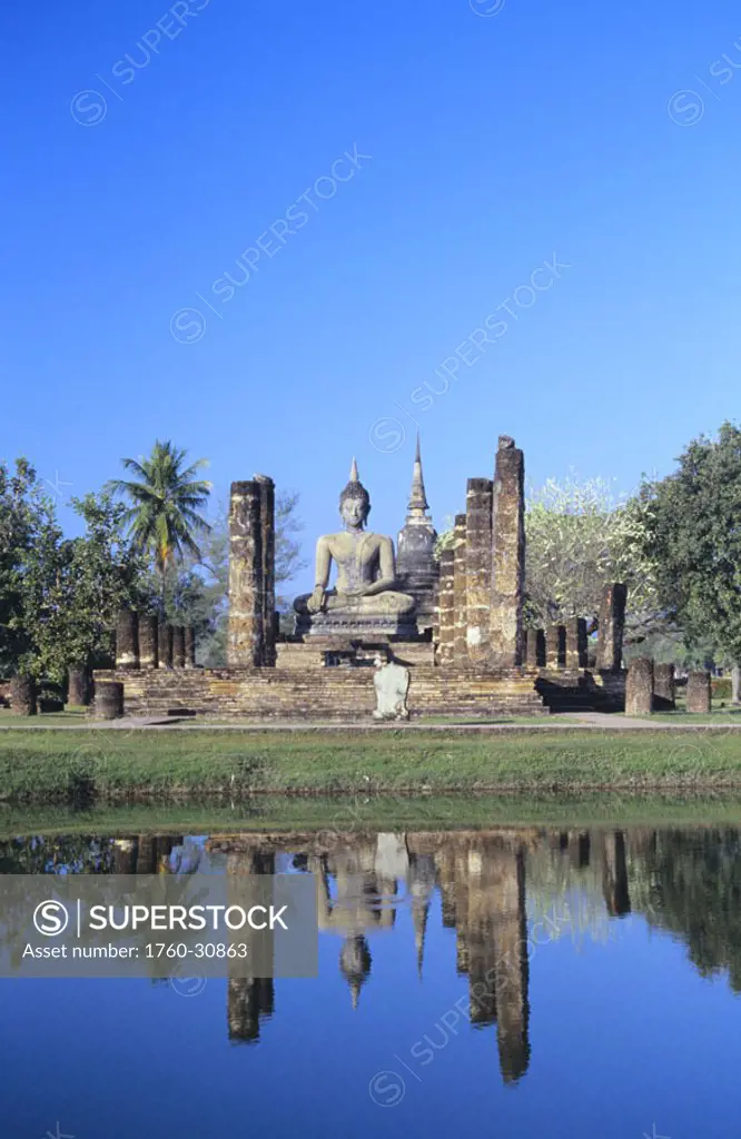 Thailand, Sukhothai, Wat Mahathat, Buddha statue and pillars, reflection in pond