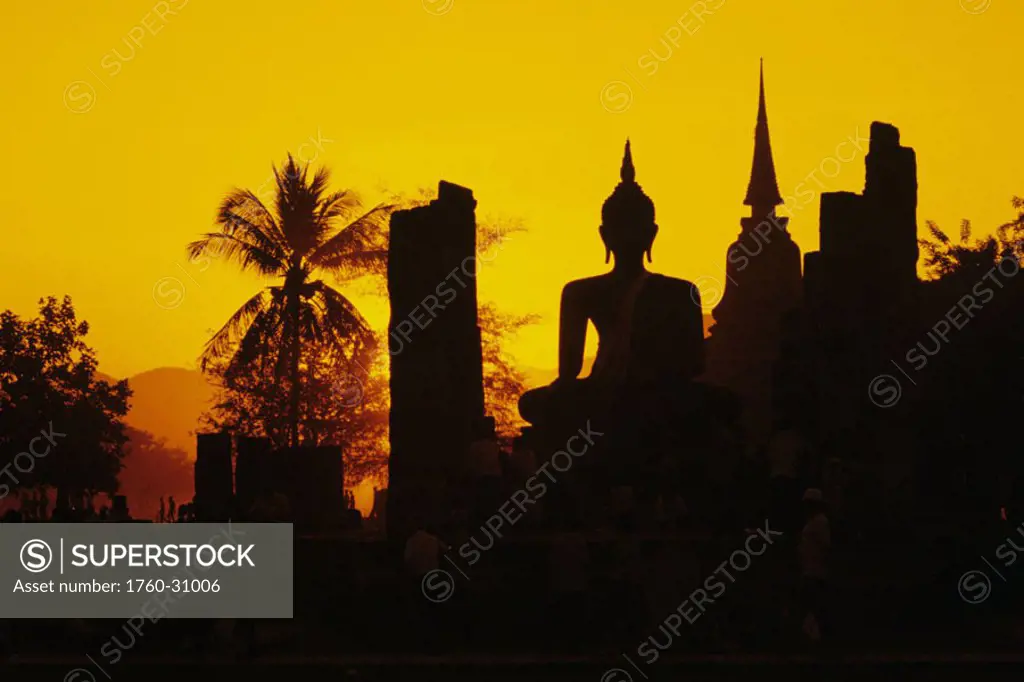 Thailand, Sukhothai, Wat Mahathat, silhouette of Buddha statue and temple against orange sky.