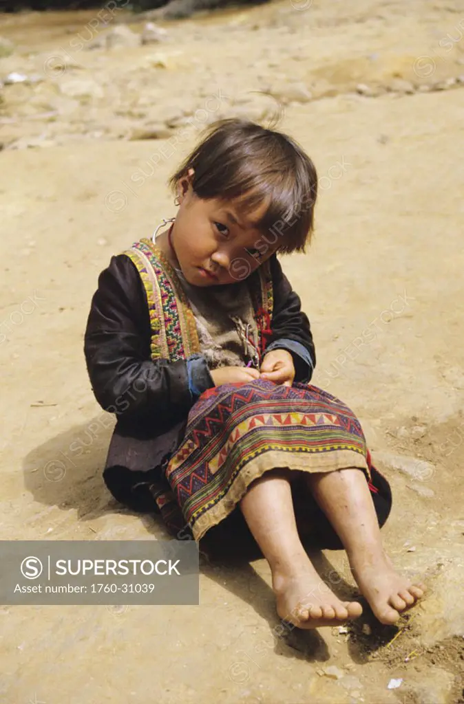 Thailand, Chiang Mai, young H´mong girl, sitting on rocks, in traditional attire.
