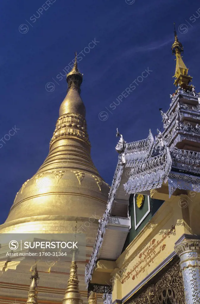 Burma (Myanmar), Yangon, Swedagon Paya, close-up of gold and silver steeple on temple pagoda against blue sky.