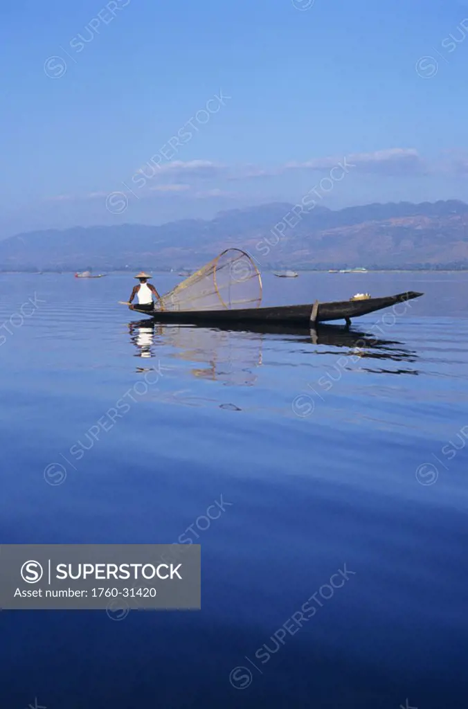 Burma (Myanmar), Inle Lake, fisherman on long flat boat, reflections on water.