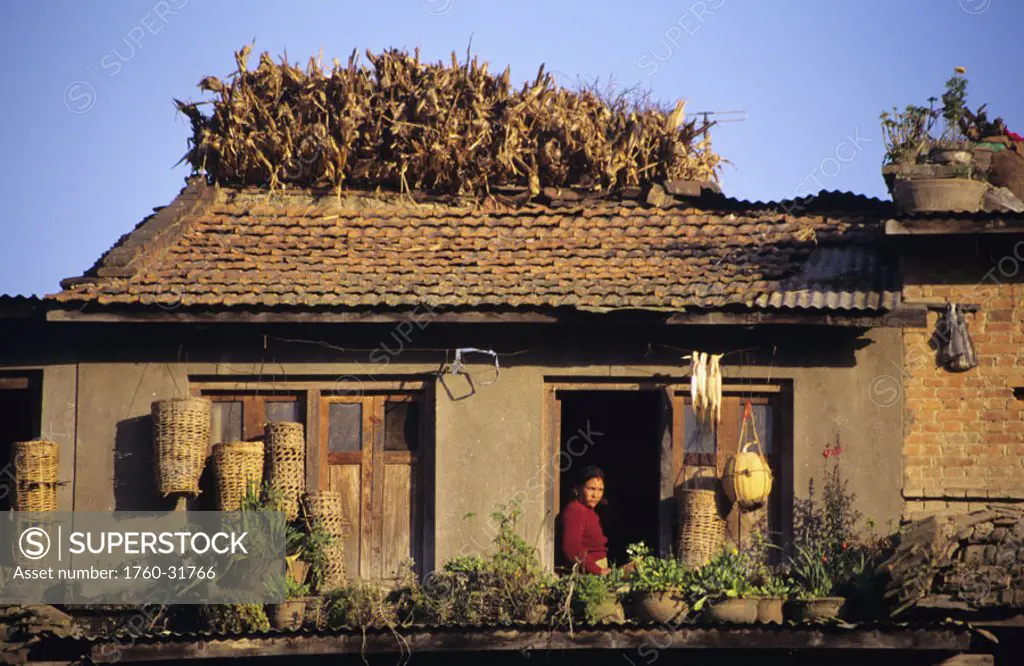 Nepal, Bungamati, Local woman in window of home, baskets and plants on sill.