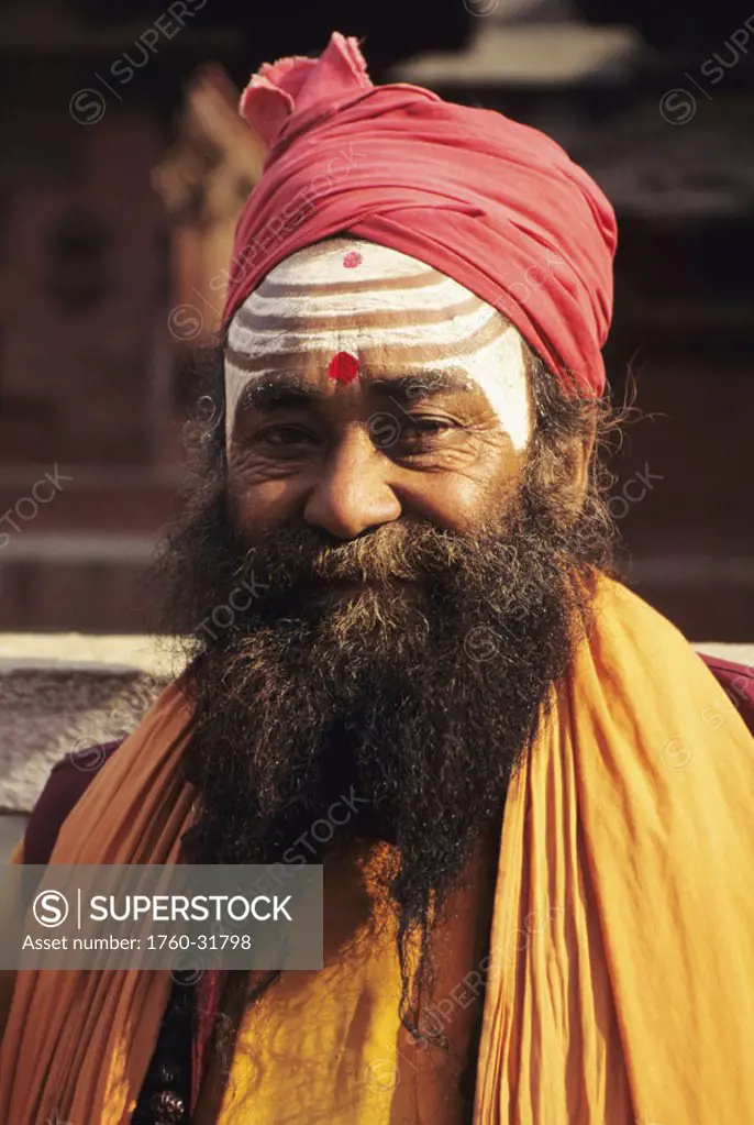 Nepal, Kathmandu Valley, headshot of Hindu holy man wearing red turban and orange scarf, painted white stripes on face.