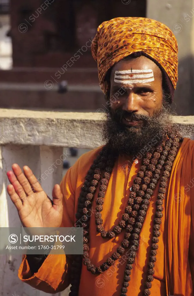 Nepal, Kathmandu Valley, Hindu holy man in orange robe and turban, smiling and gesturing with hand.
