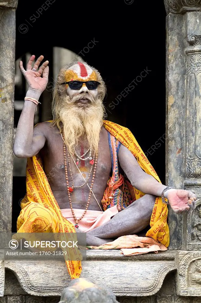 Nepal, Kathmandu, painted religious man wearing western sunglasses at Pashupatinath holy Hindu place on Bagmati River