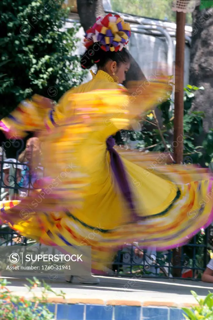Young girl in bright yellow dress and colorful hairpiece dancing, blurred action