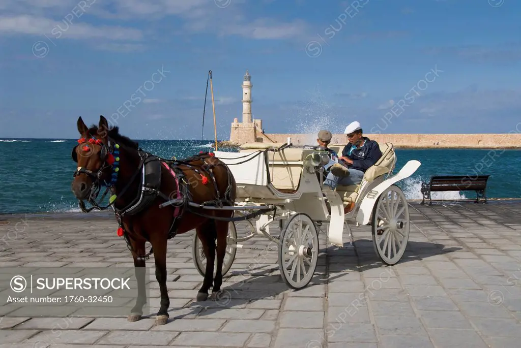 Greece, Crete, Hania, Two Men Sitting In Horse Drawn Carriage, Lighthouse And Harbor In Background.