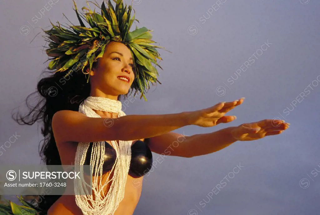 Woman hula with shell lei, coconut top, ti leaf haku arms outstretched to sky
