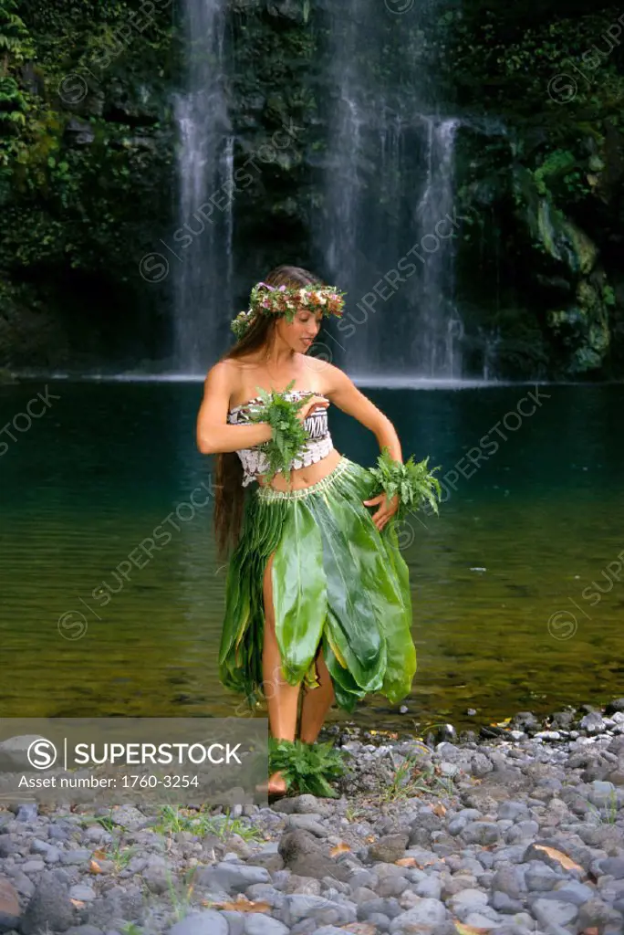 Young woman hula on rocks in front of waterfall, ti leaf skirt, flower haku C1444