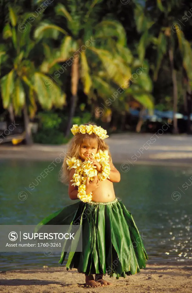 Little hula girl on beach, grass skirt, yellow lei and haku, palm tree background, water
